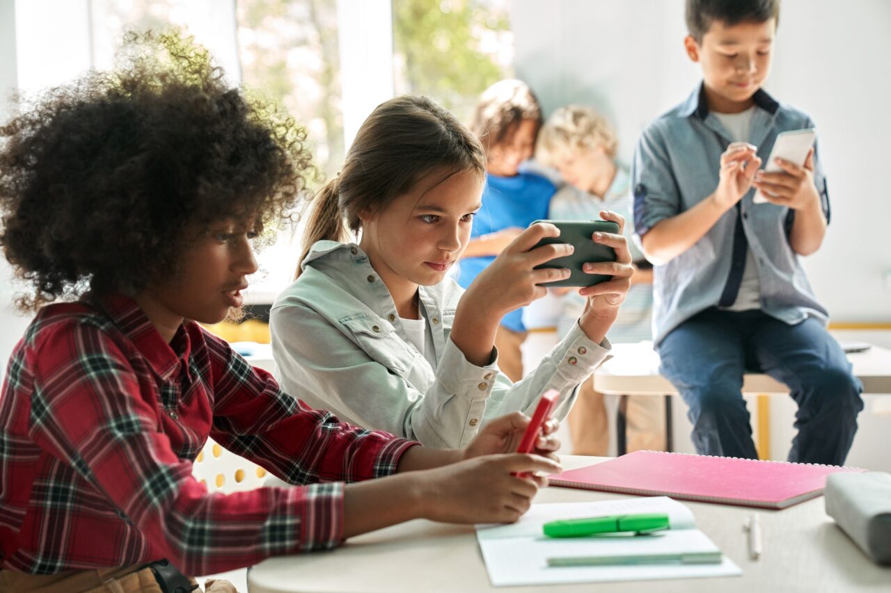 Dzieci w szkolnej klasie używają smartfonów i tabletów.