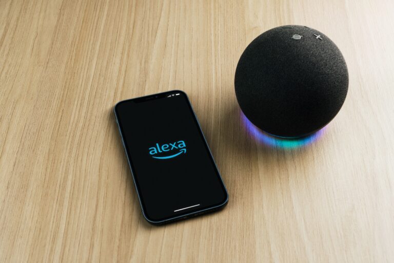 Telefon z aplikacją Alexa i inteligentny głośnik Amazon Echo na drewnianym blacie.