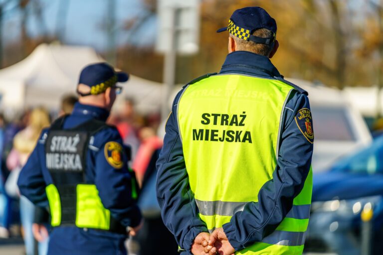 Strażnicy miejscy w kamizelkach odblaskowych podczas pracy.