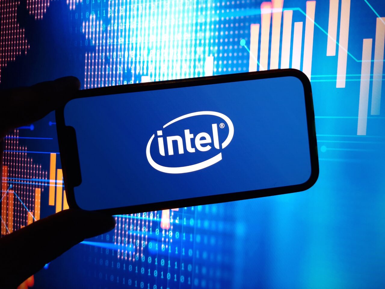 Logo firmy Intel wyświetlone na ekranie smartfona, w tle wykresy i dane cyfrowe.