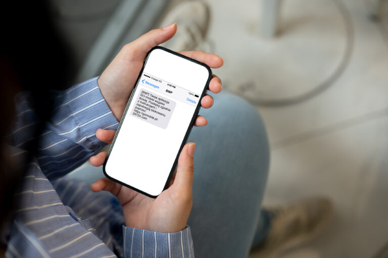 Osoba trzymająca smartfon, na ekranie widoczna jest wiadomość SMS o treści "BNP. Twoja aplikacja GO!mobile wygasa " wraz z linkiem do strony internetowej.