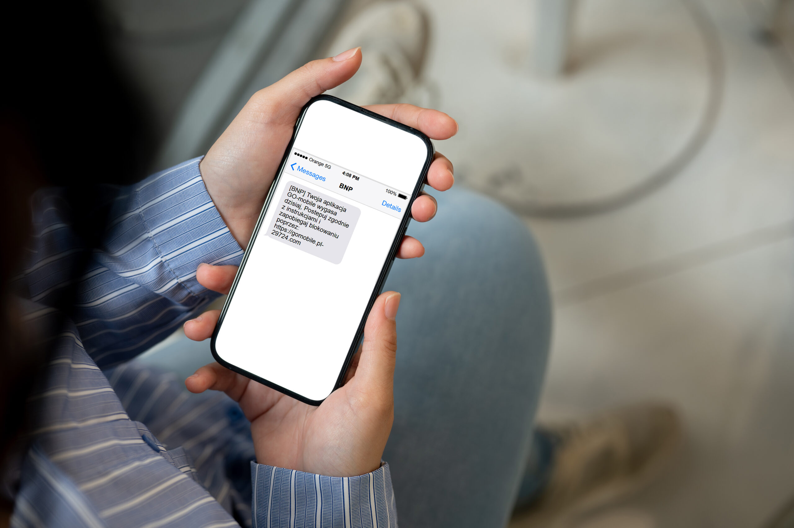 Osoba trzymająca smartfon, na ekranie widoczna jest wiadomość SMS o treści "BNP. Twoja aplikacja GO!mobile wygasa " wraz z linkiem do strony internetowej.