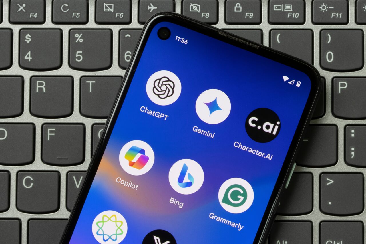 Smartfon z ikonami aplikacji ChatGPT, Gemini, Character.ai, Copilot, Bing oraz Grammarly, leżący na klawiaturze laptopa. Polacy chcą AI w smartfonach.