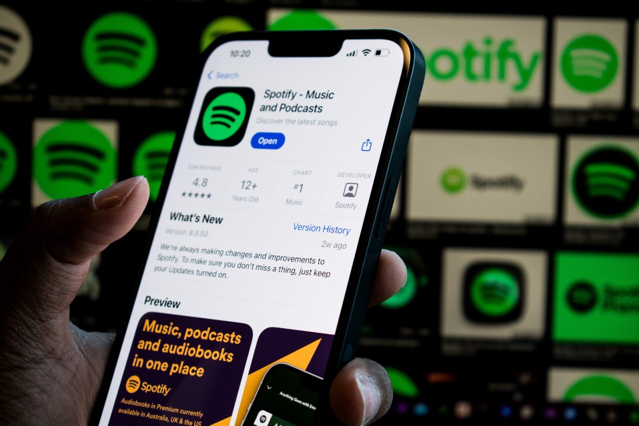 Osoba trzymająca smartfona z otwartą aplikacją Spotify na ekranie w tle z logo Spotify.