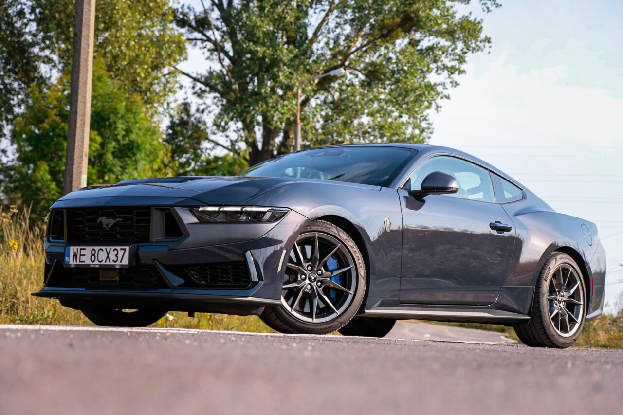 Test Ford Mustang Dark Horse stojący na drodze w otoczeniu drzew.