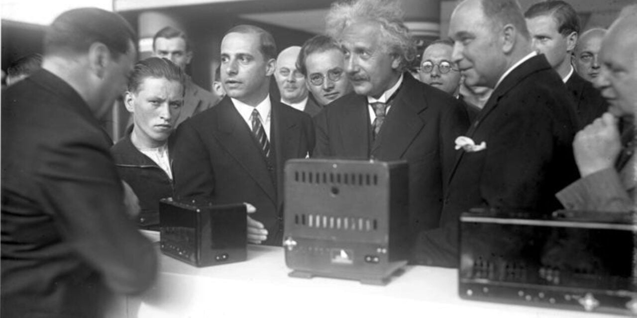 Targi IFA: Albert Einstein i grupa mężczyzn w garniturach patrzy na dwa urządzenia elektroniczne na stole.