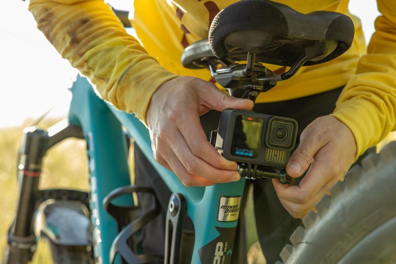 Rowerzysta w żółtej koszulce montuje kamerę GoPro pod siodełkiem niebieskiego roweru.