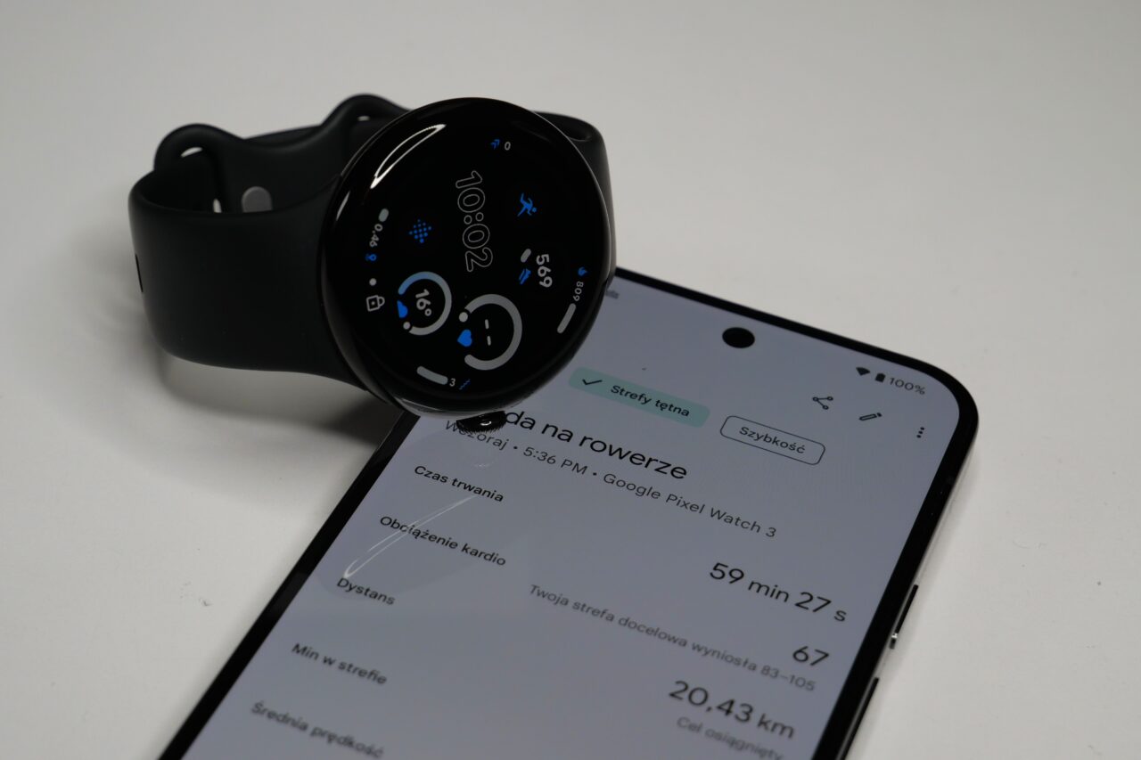 Czarny smartwatch na bicie nad ekranem smartfona pokazującego szczegóły aktywności rowerowej.