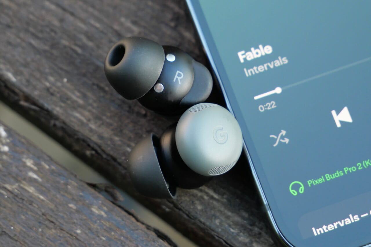 Douszne słuchawki Pixel Buds Pro obok smartfona z odtwarzaczem muzyki.