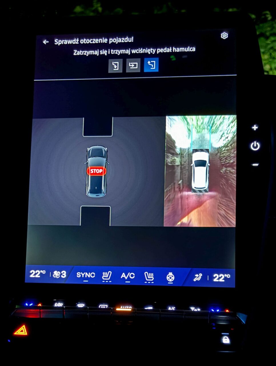 Ekran systemu samochodowego z kamerą cofania, znak "STOP" i informacje o otoczeniu pojazdu.