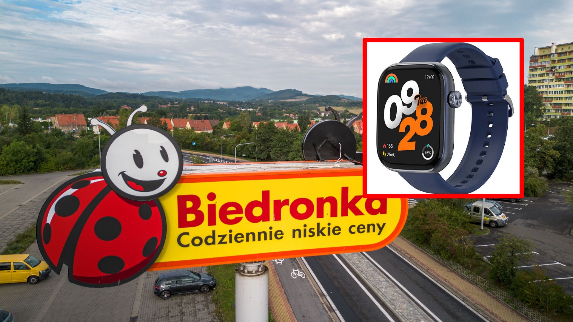 Szyld sklepu Biedronka z napisem "Codziennie niskie ceny", na tle zielonych wzgórz i osiedla mieszkaniowego. W prawym górnym rogu wstawka z obrazem „Apple Watch” o granatowym pasku.