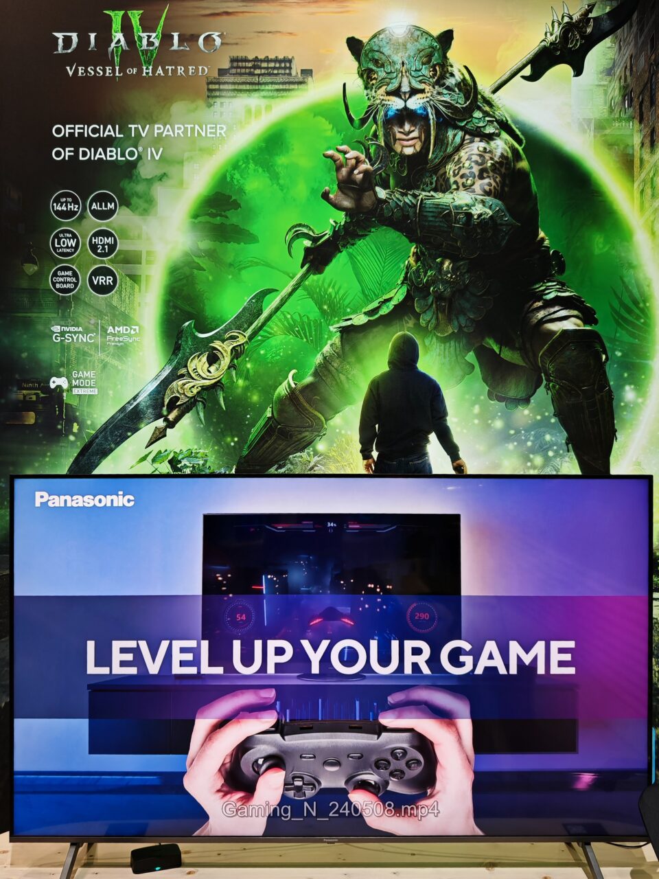 Plakat gry Diablo IV z wojownikiem w hełmie kota i telewizor Panasonic z tekstem "LEVEL UP YOUR GAME" i kontrolerem do gier.