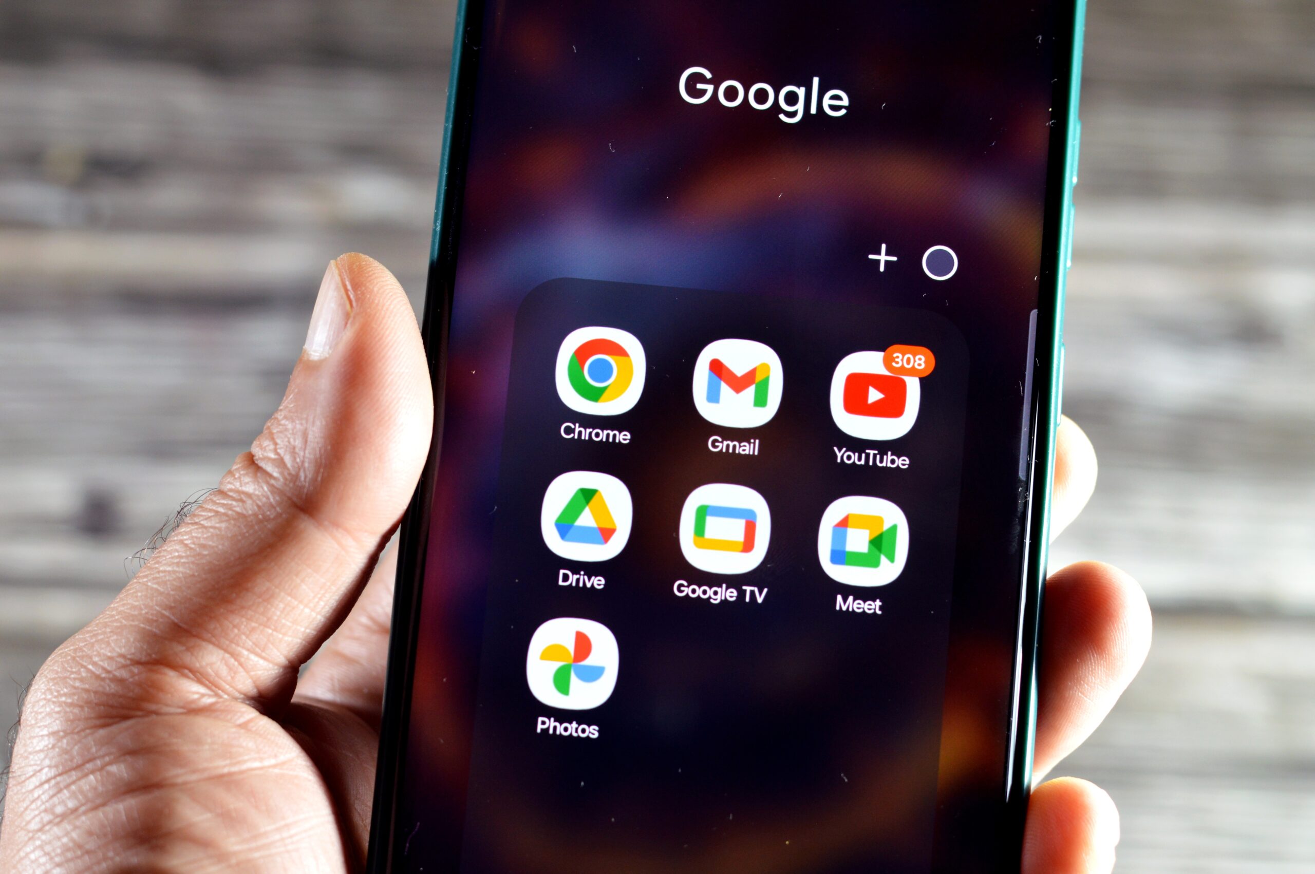 Ręka trzyma smartfon z otwartym folderem "Google" zawierającym aplikacje: Chrome, Gmail, YouTube, Drive, Google TV, Meet i Photos.