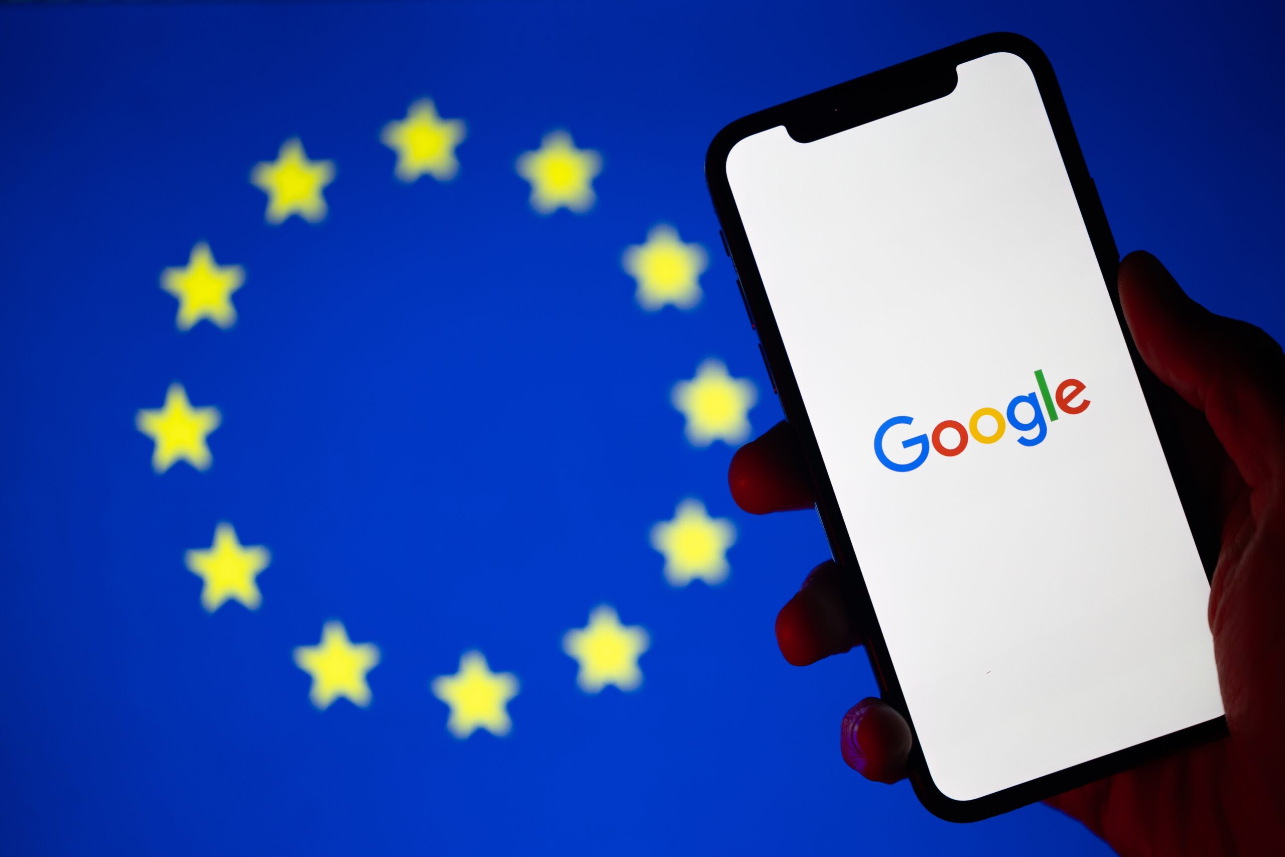 Flaga Unii Europejskiej w tle z logo Google na ekranie smartfona w pierwszym planie.