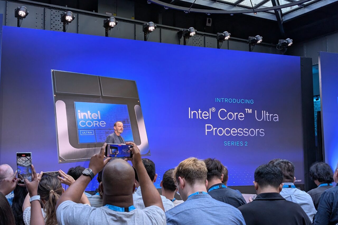 Prezentacja procesorów Intel Core Ultra Series 2. Przemawiający mężczyzna na scenie za nim duży ekran z logiem Intel Core. Przed sceną grupa ludzi robiących zdjęcia.