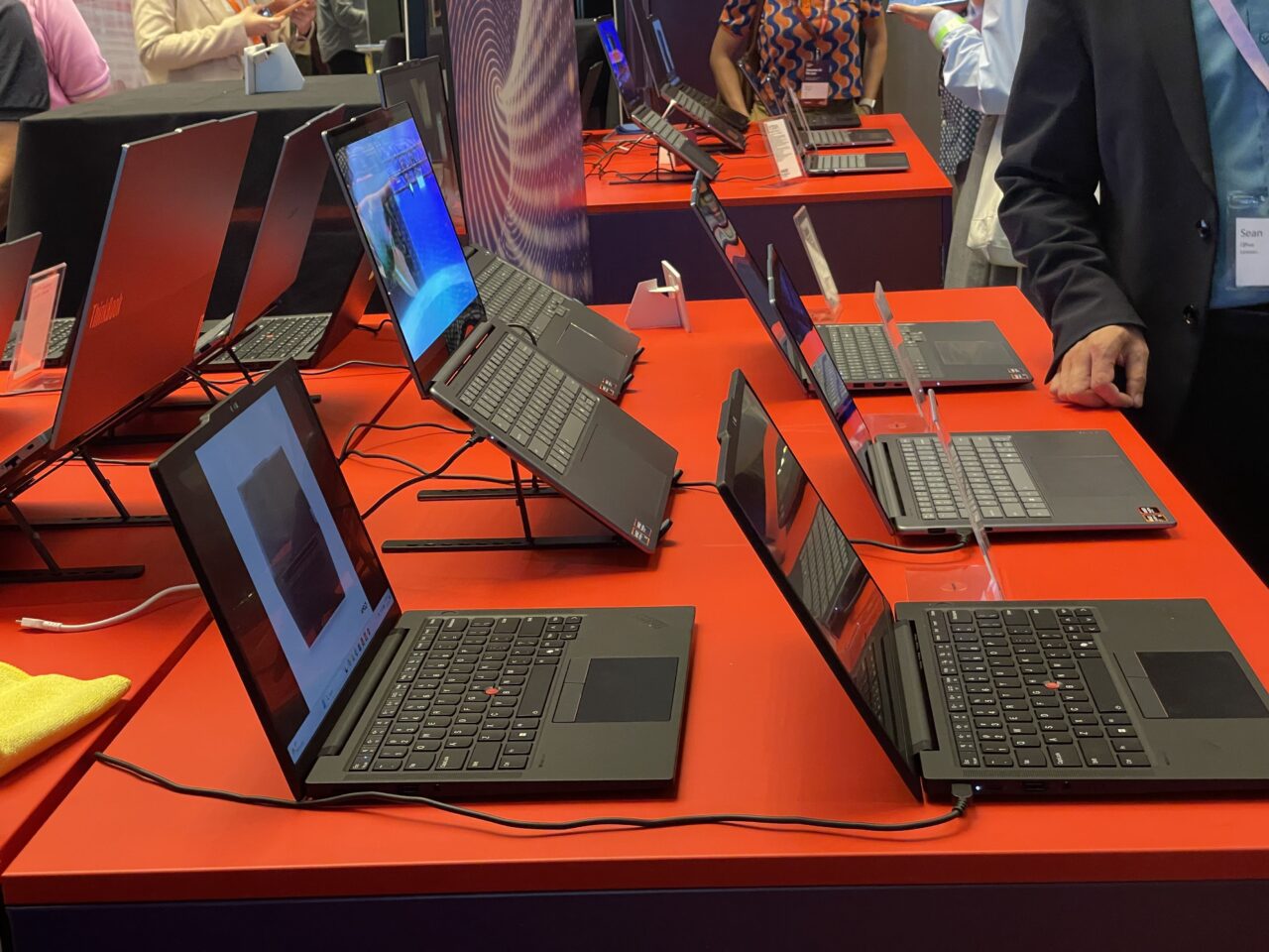 Laptopy Lenovo na czerwonym stole wystawowym, ludzie w tle. Premiera Aura Edition na IFA 2024