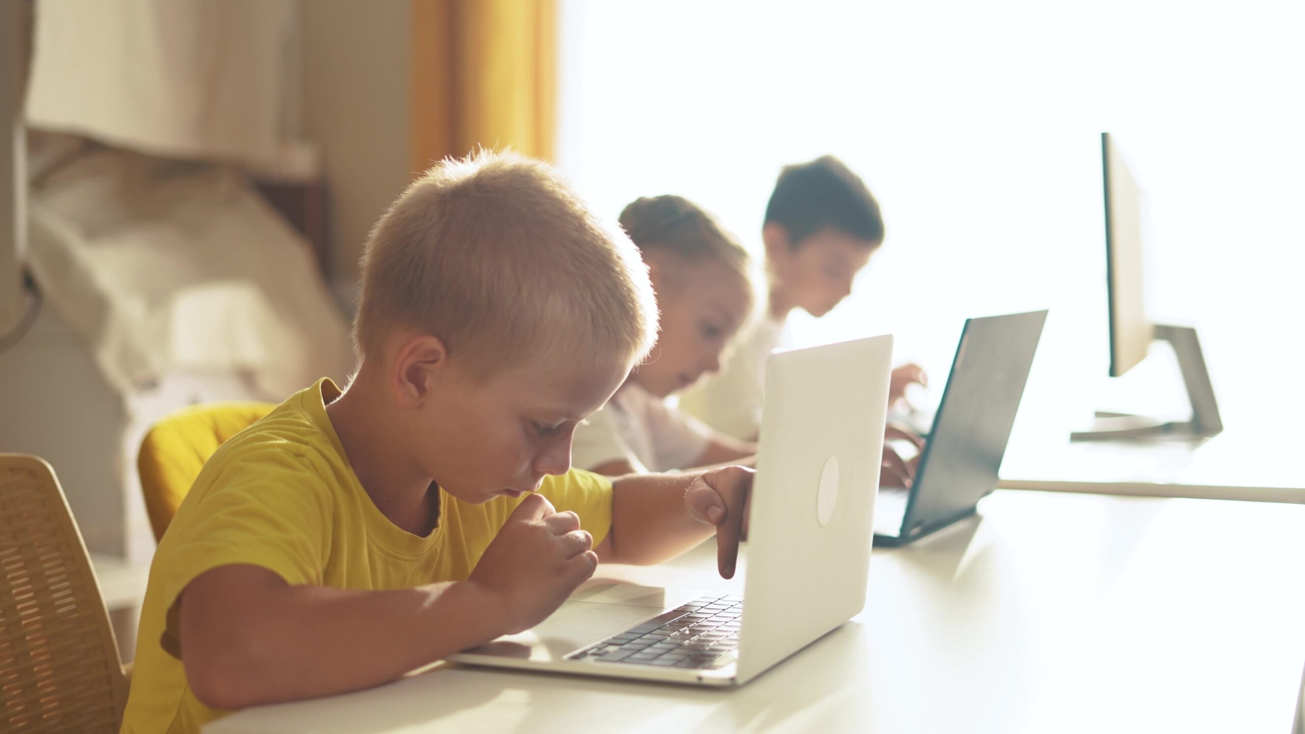 Dzieci siedzące przy biurkach i pracujące na laptopach.