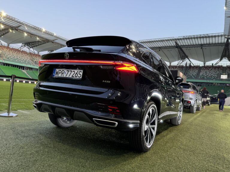 Czarne SUV marki MG HS Plug-in z rejestracją WPR 7726S na stadionie piłkarskim.