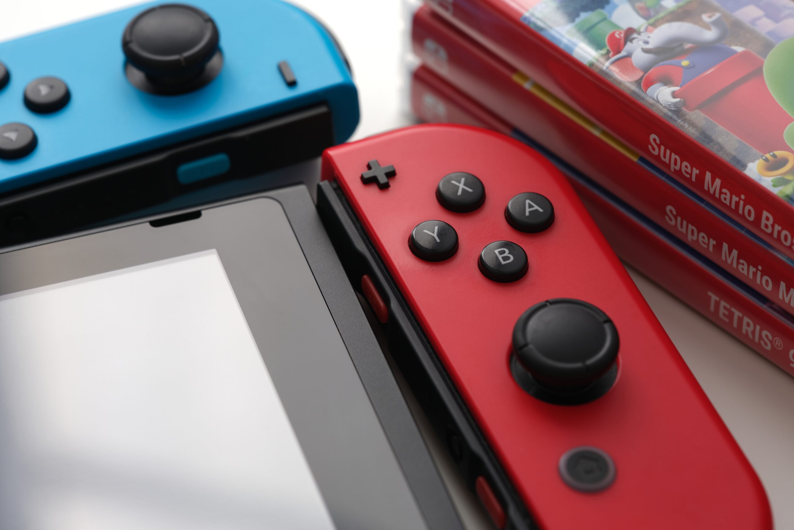 Konsola Nintendo Switch z kolorowymi kontrolerami Joy-Con oraz kilka pudełek z grami, m.in. "Super Mario Bros." i "Tetris". Będzie kompatybilna z Nintendo Switch 2