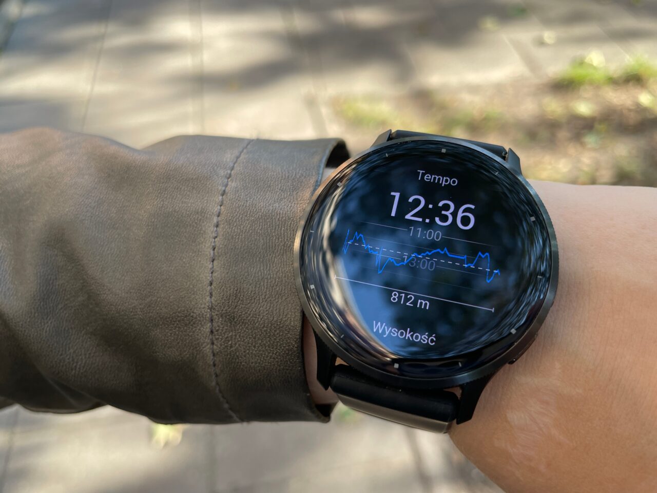 Smartwatch na nadgarstku pokazujący godz. 12:36, tempo i wysokość 812 m.