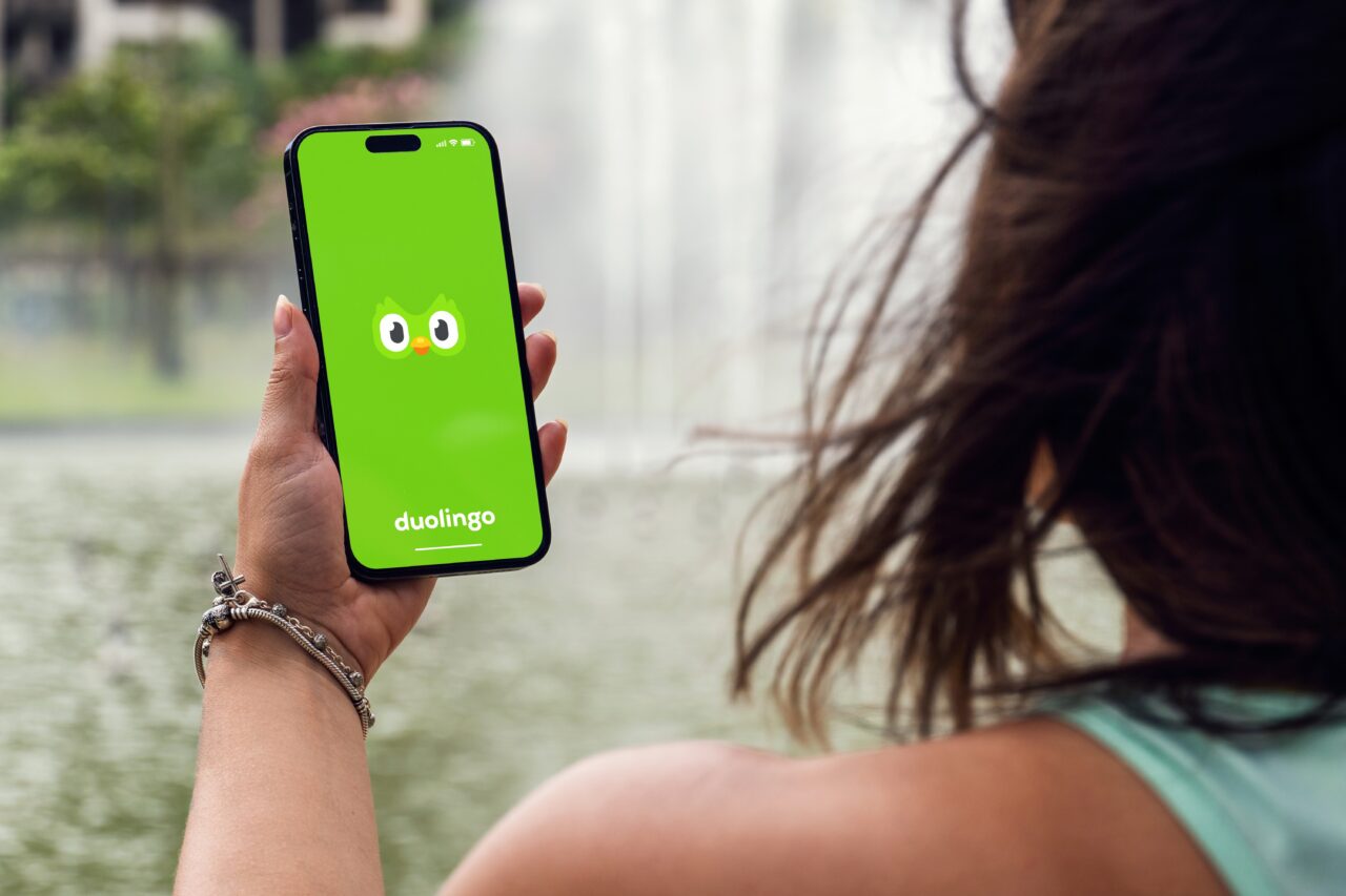 Osoba trzymająca telefon z włączoną aplikacją Duolingo na tle fontanny.