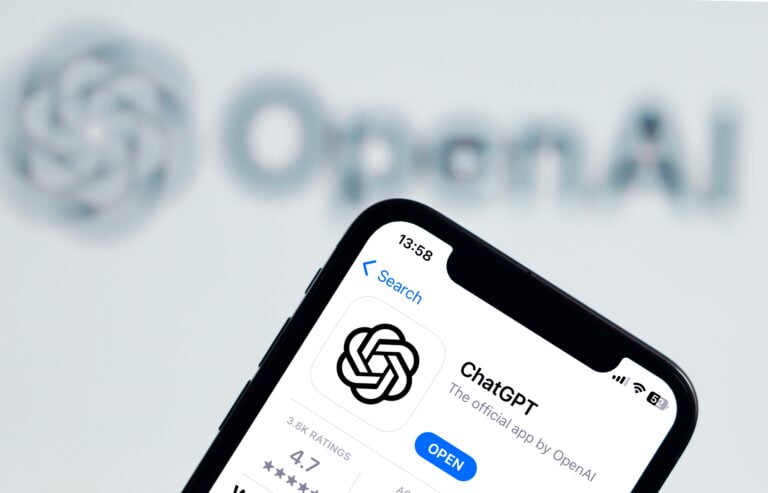 Ekran smartfona z aplikacją ChatGPT, w tle rozmyte logo OpenAI.