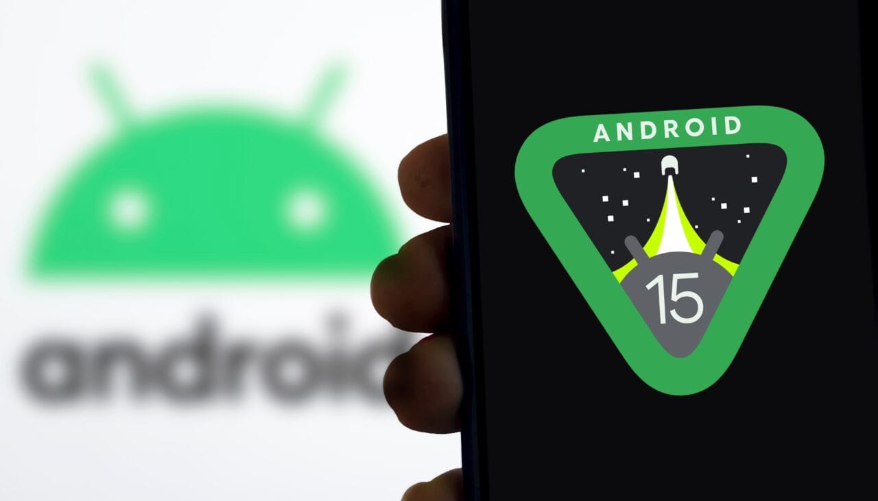 Logo Android 15, systemu, który zostanie zastąpiony przez Android 16 na ekranie telefonu, w tle rozmazany zielony robocik Androida.