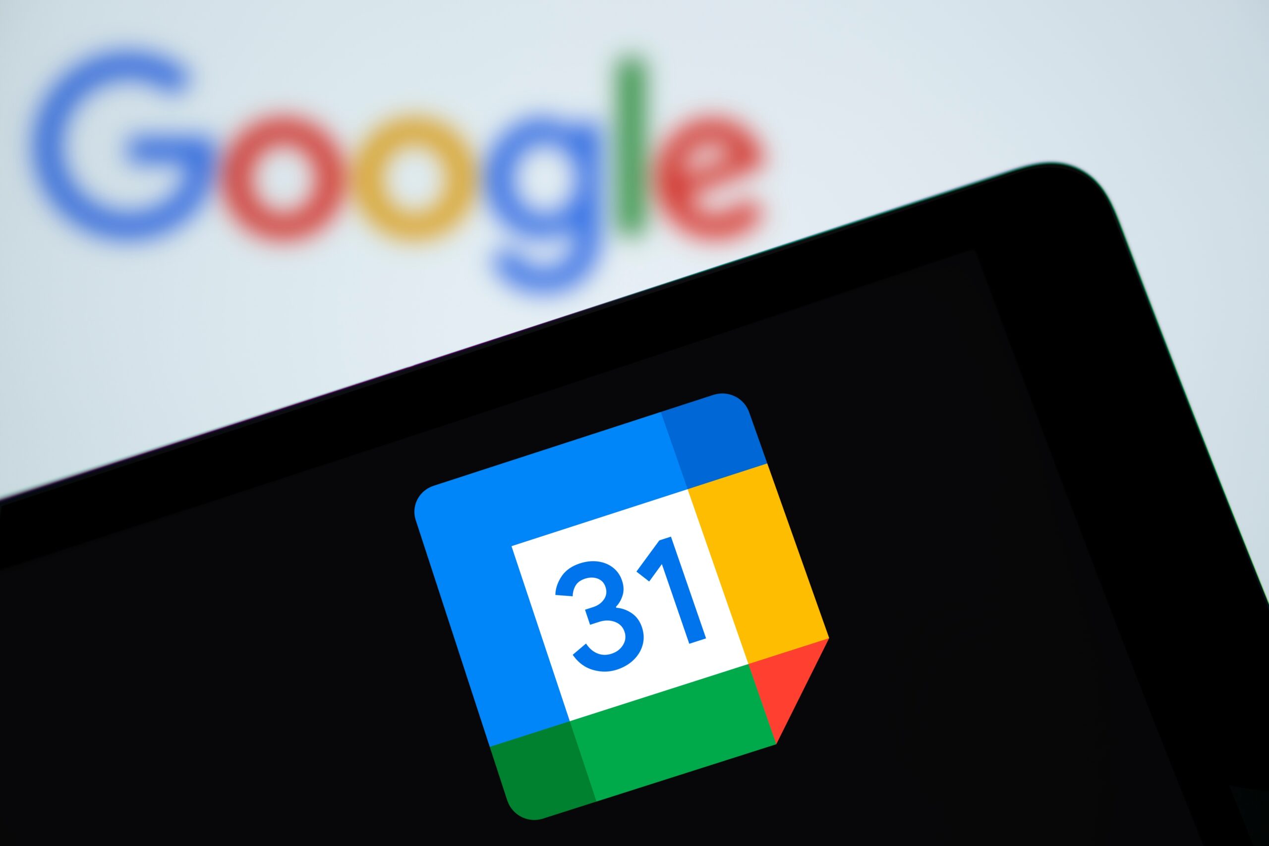 Ikona aplikacji Google Calendar na ekranie urządzenia, z rozmytym logo Google w tle.