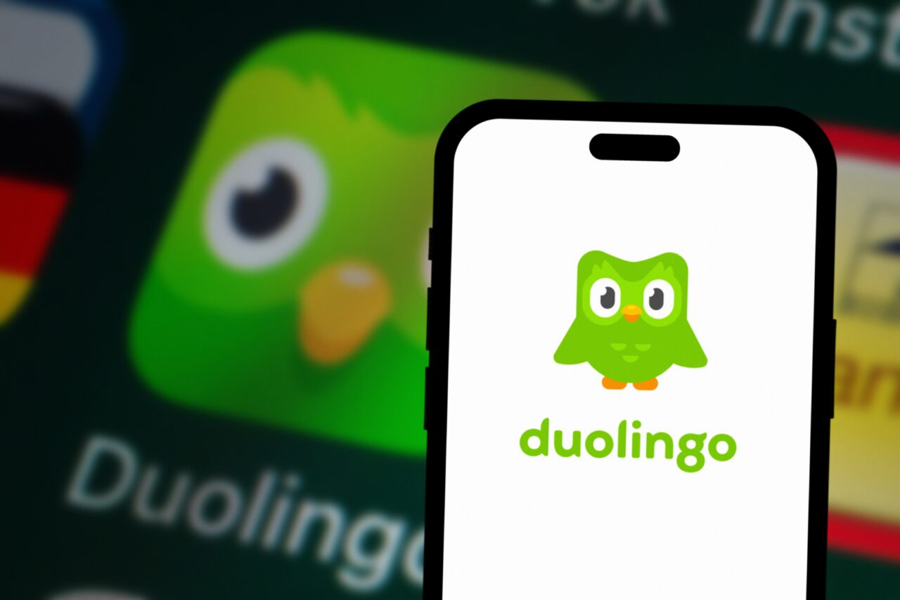 Logo aplikacji Duolingo na ekranie smartfona na tle rozmytego obrazu ikony aplikacji.