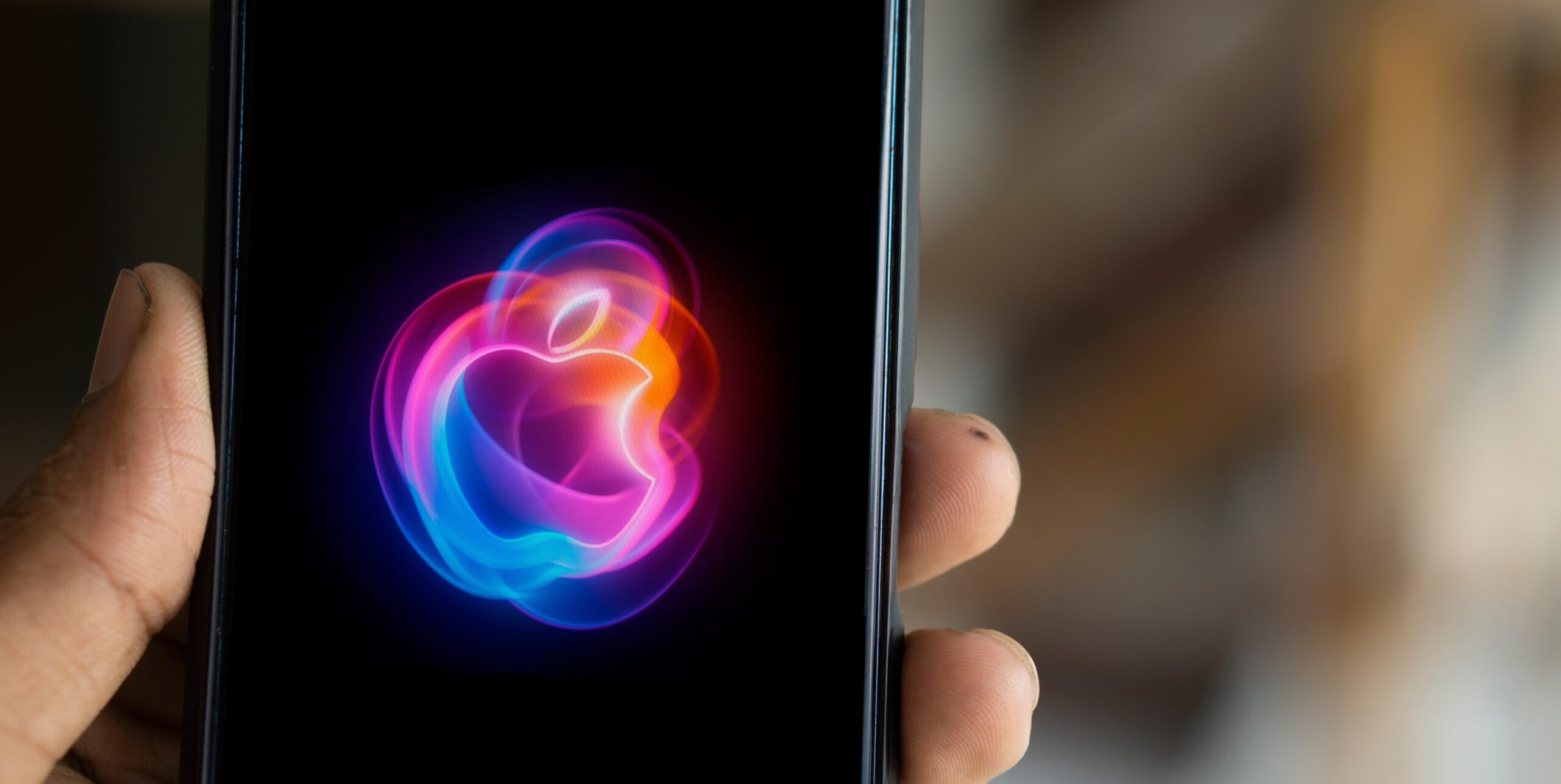 Telefon trzymany w dłoni z wyświetlaną na ekranie kolorową iluminacją w kształcie logo Apple.