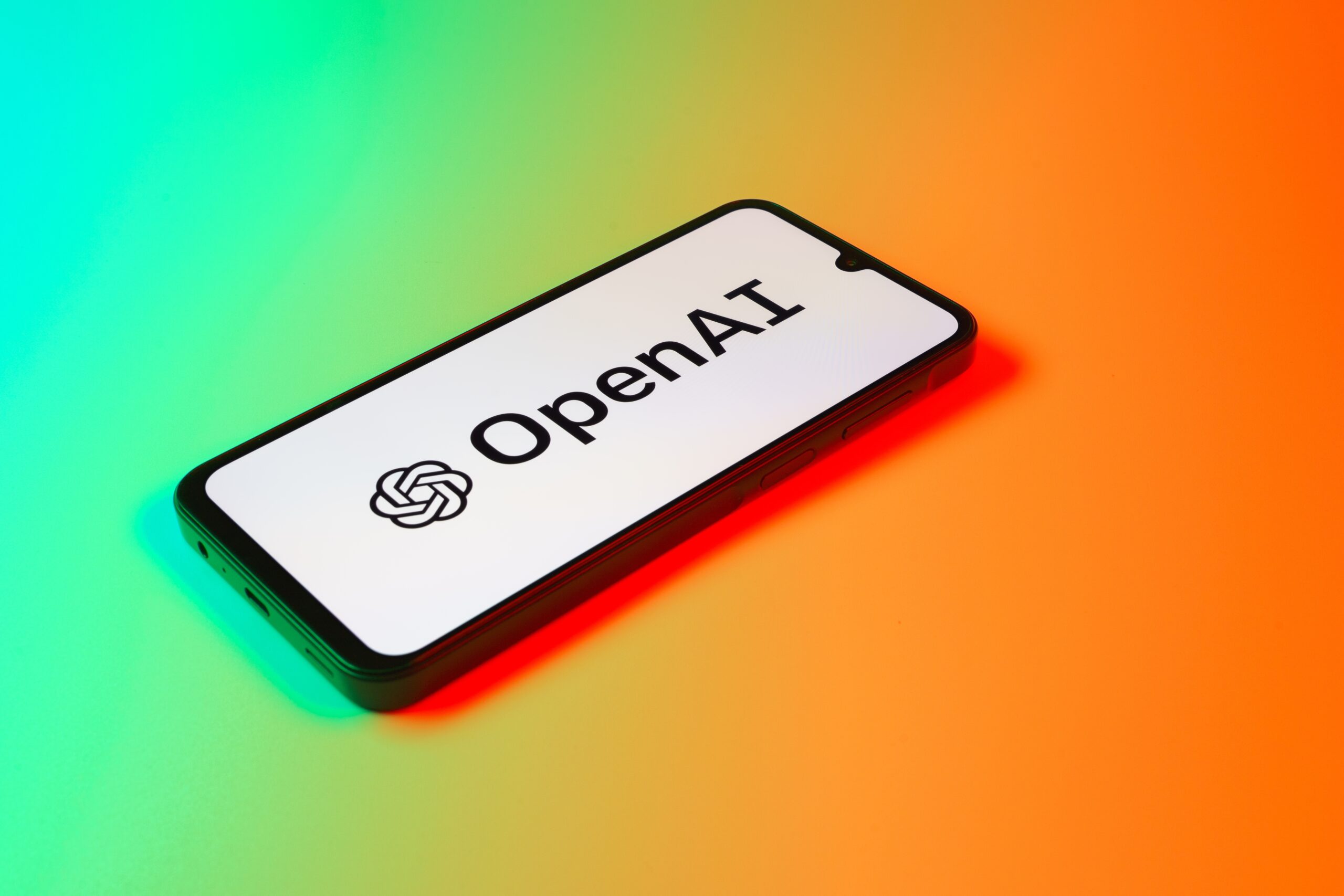 Smartfon z logo OpenAI na ekranie, leżący na powierzchni z gradientowym kolorowym tłem.