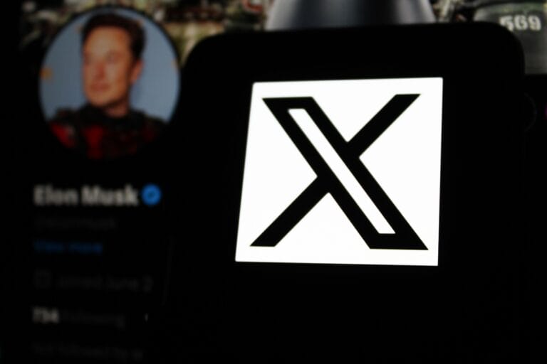 Logo "X" na ekranie telefonu, w tle rozmyty profil użytkownika na Twitterze.