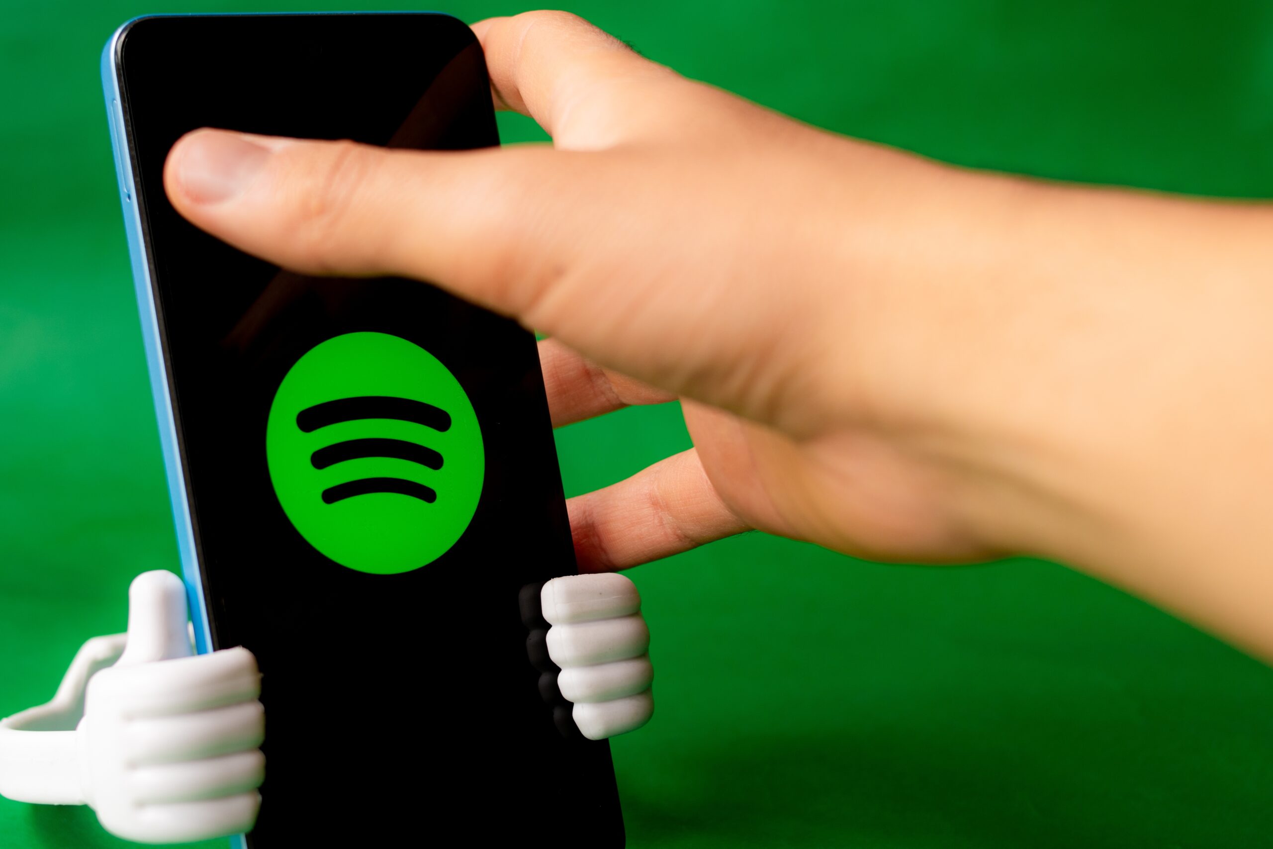 Smartfon z logo Spotify trzymany przez rękę na zielonym tle.