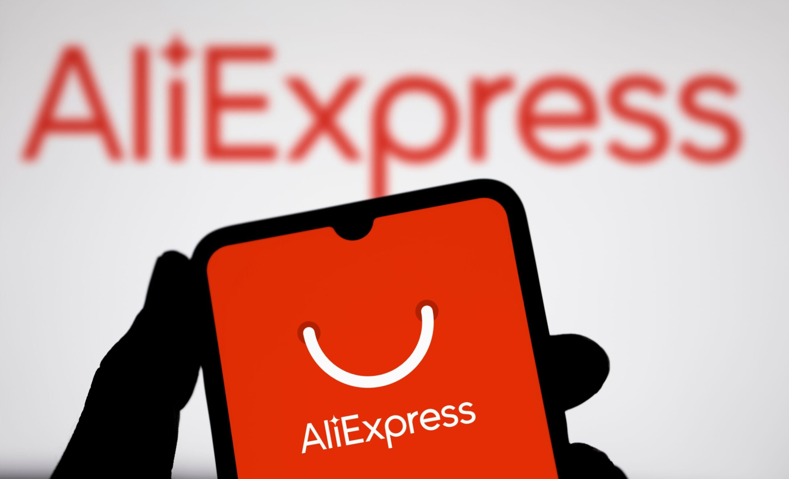 Logo AliExpress na ekranie telefonu komórkowego, w tle rozmyte większe logo AliExpress.