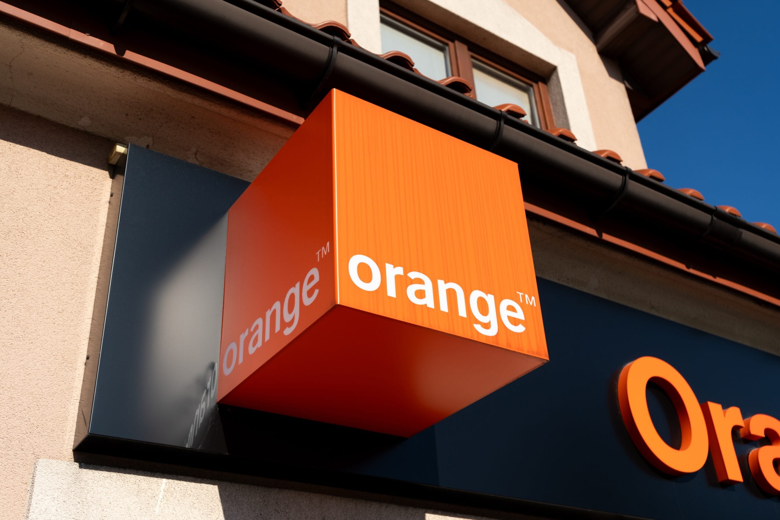 Pomarańczowy szyld z logo Orange na budynku.